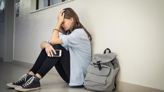 Unhappy girl sitting on floor holding mobile phone