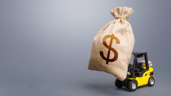 Forklift carrying a dollar money bag