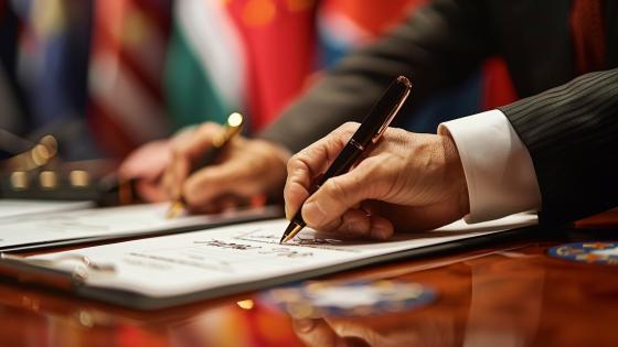 hand of someone signing trade agreement in front of flags