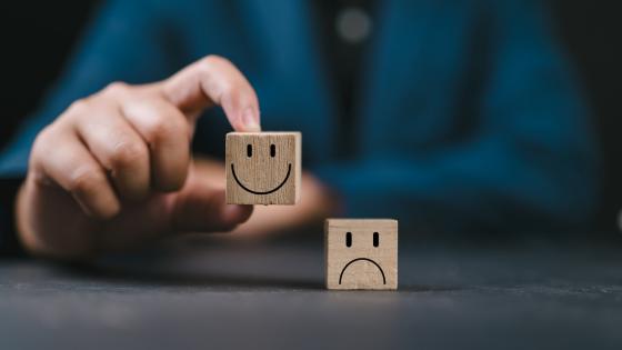 Hand holding smiley happy face on wooden cube and unhappy sad emotion on the floor.
